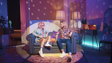 caucasian man with long hair and caucasian stylish woman in sunglasses talking while sitting on couch in a retro party at home