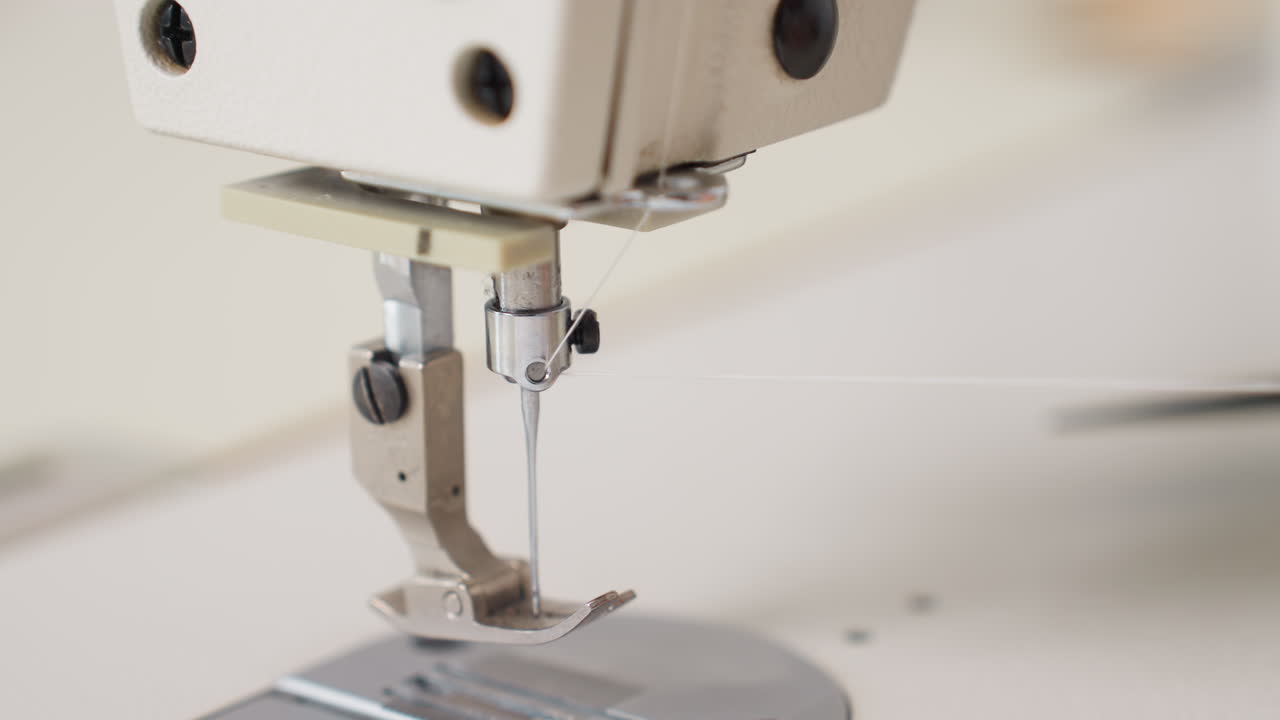 Close up view of designer skillfully adjusting thread on electric sewing machine, highlighting needle mechanism, metallic foot, and precise tension, capturing professional technique environment