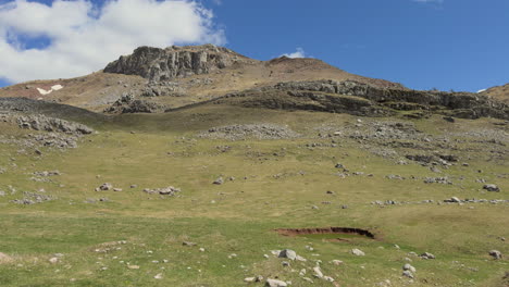 a scenic mountain-top view captured from a moving car, showcasing a rugged landscape of rocky terrain and low grass-covered fields. sunny day, slow motion