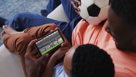 composite of father and son at home watching rugby match on smartphone