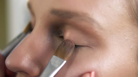 the make-up artist puts light shiny eyeshadow on a model's eyelids using two professional brushes. close up. make up process