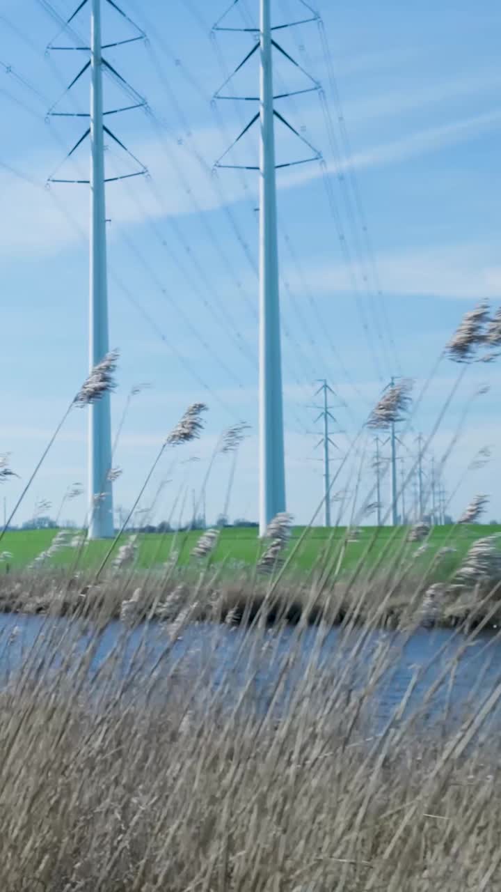 Høyspentmaster og kraftledninger over grønn åker og kanal