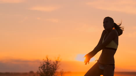 SLOW-MOTION-LOW-ANGLE-CLOSE-UP-SUN-FLARE:-Athletic-girl-playing-beach-volleyball-jumps-in-the-air-and-strikes-the-ball-over-the-net-on-a-beautiful-summer-evening.-Caucasian-woman-score-a-point.