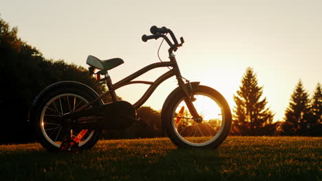 children's bicycle standing on a green lawn on the background of the setting sun concept - children'