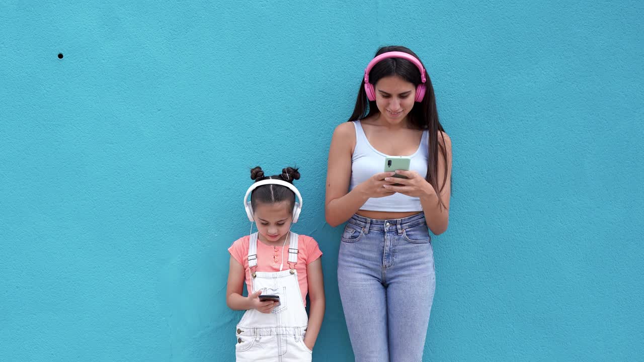 una adolescente y su hermana pequeña usando una aplicación en línea en su teléfono inteligente y escuchando una lista de reproducción de música