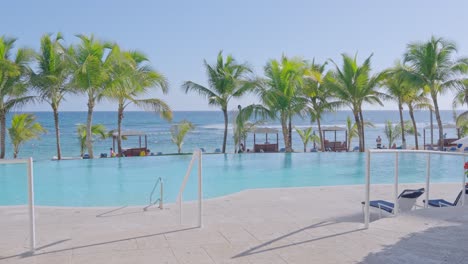 Piscina-Vacía-Y-Hermoso-Mar-Caribe-En-Segundo-Plano-Durante-El-Día-Soleado-En-El-Complejo-Hotelero---Gente-Descansando-En-La-Playa-En-El-Océano