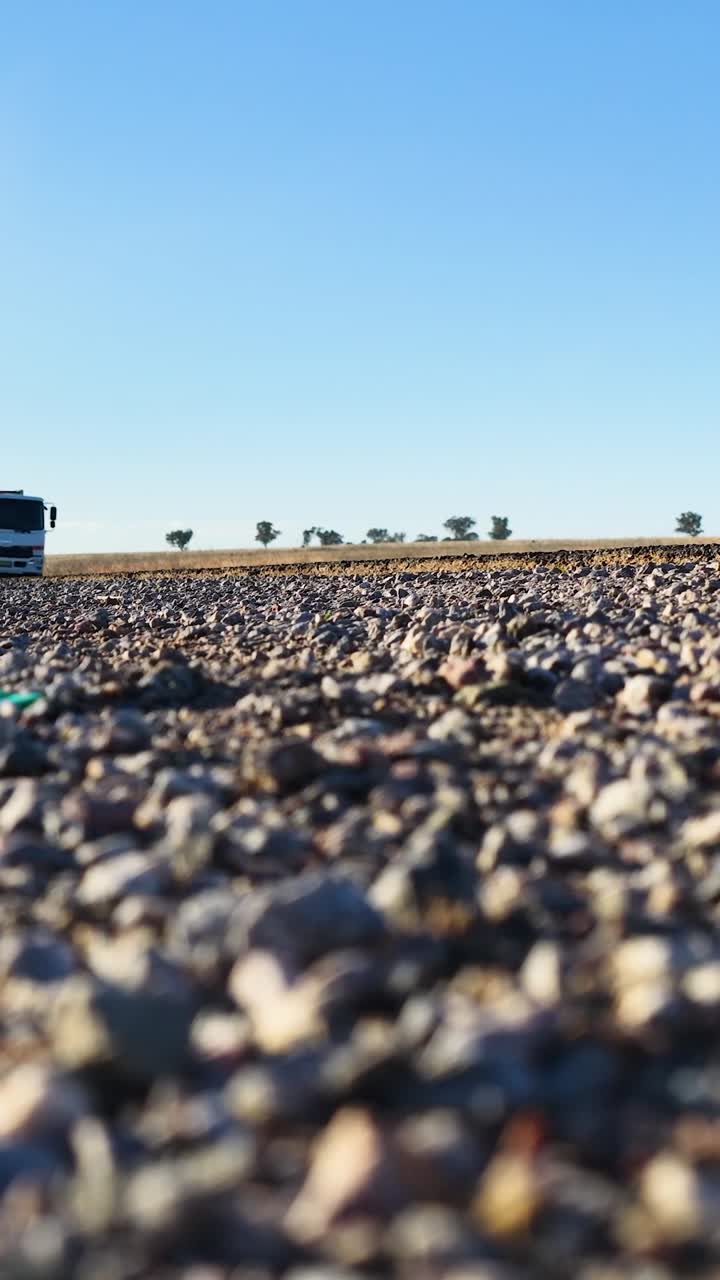 Prospettiva a livello del suolo di veicoli commerciali e un'auto che viaggiano lungo una strada sterrata rurale
