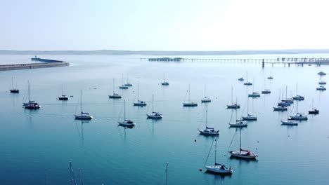 Sonnige-Holyhead-Harbour-Wellenbrecher-Seeyachten,-Die-Entlang-Einer-Transparenten,-Ruhigen,-Blauen-Küstenlinie-Aus-Der-Vogelperspektive-Angedockt-Sind