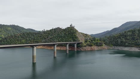 flying overhead, a drone captures the don pedro reservoir bridge stretching across the vast lake. shot on a dji air 3s.