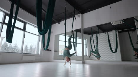 a young beautiful woman performs exercises on a hammock from aero yoga. a woman in the afternoon in front of the mirror in the hall performs stretching alone