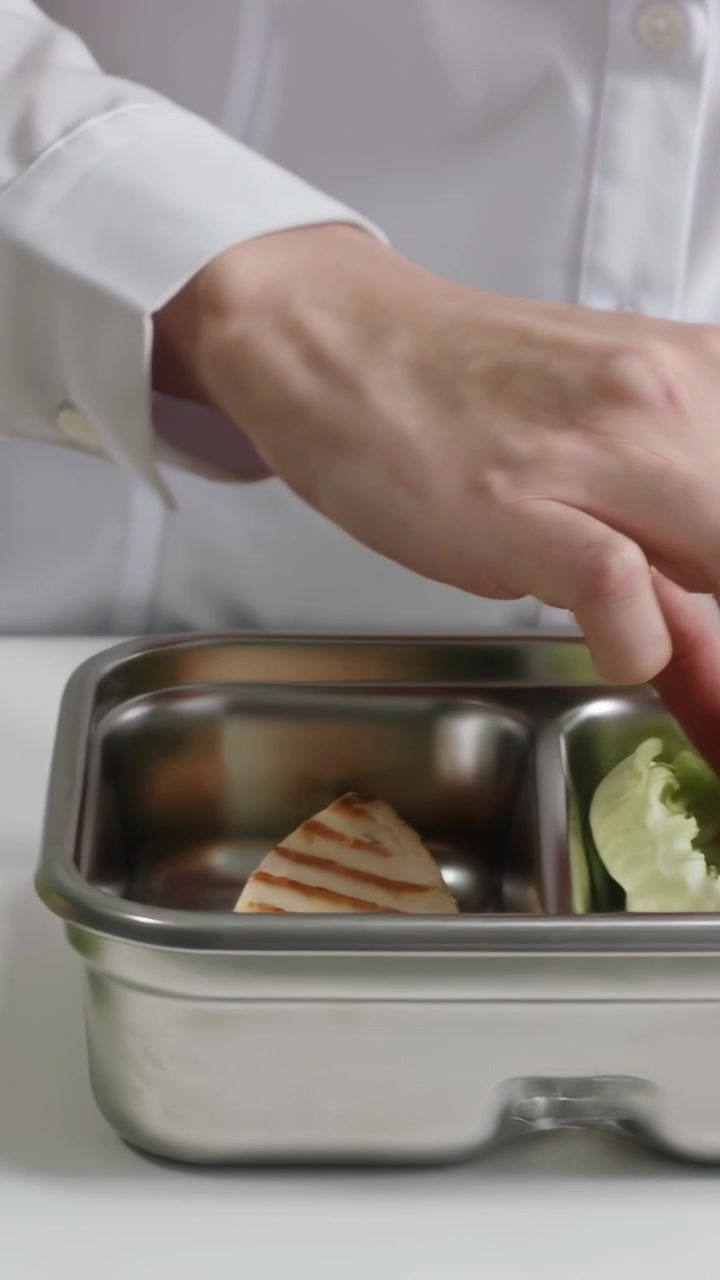 Vertikales Video: Kochhände legen gegrilltes Hähnchen in Stahlpfanne, verpacken Mittagessen, in weißer Kochjacke.