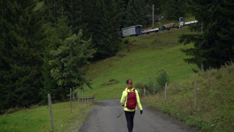 Woman-hiking-down-dirt-road-and-supply-train-passes-in-Grindelwald-Switzerland