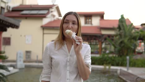 retrato de una hermosa joven positiva comiendo helado en el fondo de casas borrosas