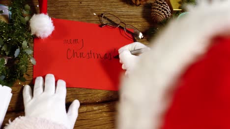 santa claus writing merry christmas on card