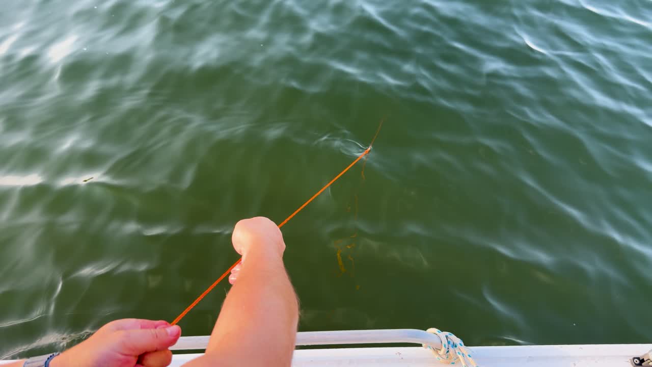 Person retrieves empty orange fishing line from water, bright daylight, handheld camera, marine environment