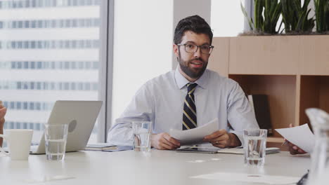 Hombre-De-Negocios-Con-Papeleo-Sentado-En-La-Mesa-Reuniéndose-Con-Colegas-En-Una-Oficina-Moderna