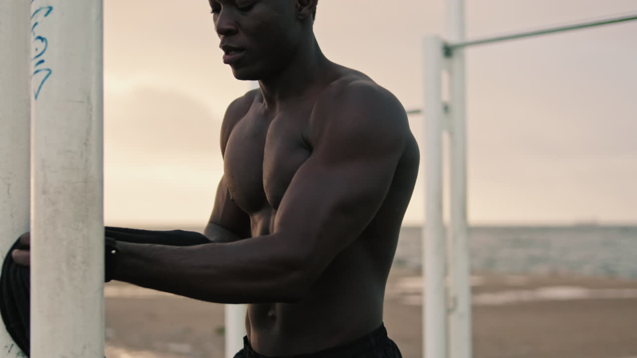 Uomo nero muscoloso si toglie la maglietta in una palestra all'aperto in spiaggia.