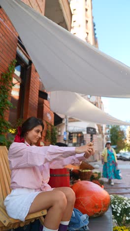 woman taking selfie outdoors by cafe with pumpkins