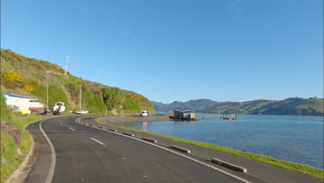 el pov del coche conduciendo por la carretera costera a lo largo del mar azul en la península de dunedin, otago, nueva zelanda