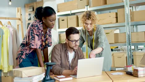 equipo de diseñadores multiétnicos hablando mientras navega en línea buscando en internet en una computadora portátil en una tienda de ropa de moda