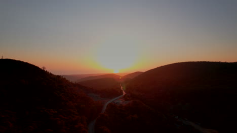 drone shot of road through italian mountains leading to golden sunset on horizon