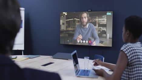 diversas personas de negocios en videollamada con un colega caucásico en la pantalla de televisión