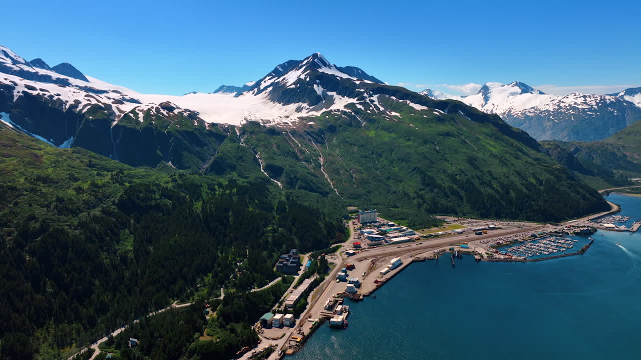 Little town at the foot of the verdant mountains on the river waterfront. Snow lies on the tops of the rocks. Alaska, USA