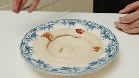 Chef decorating hummus plate with grinded paprika and parsley