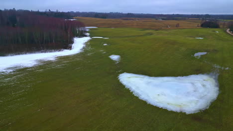 Paisaje-Aéreo-De-Drones-De-Caminos-Congelados-En-Una-Cancha-Verde-Con-árboles-Oscuros-Secos-Pinos-Horizonte-Nublado-Invierno-Otoñal,-Cámara-Lenta-Superior-Estableciendo-Tiro