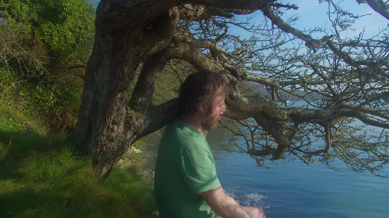 Man Sitting Under Shade of Lakeside Tree on Sunny Afternoon Meditating - close up