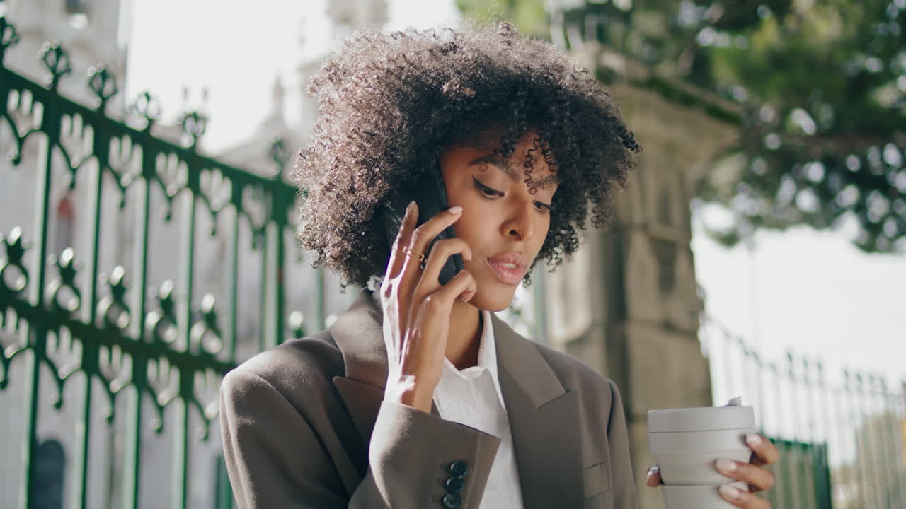Black hair woman calling mobile holding coffee outdoors closeup. Lady talking