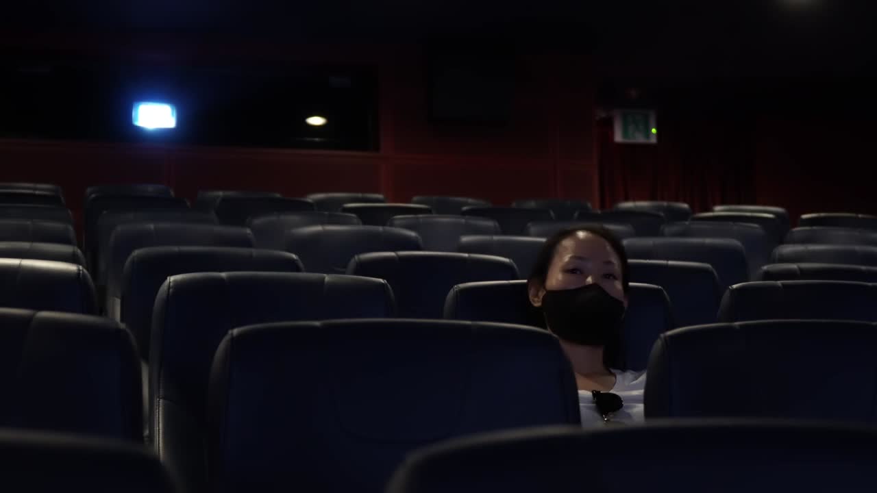 Front View Of An Exhausted Woman Sitting Alone In The Cinema And Watching Movie After A Long Day. wide