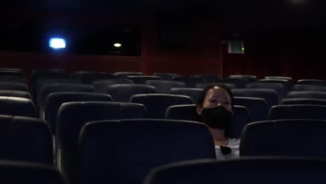 front view of an exhausted woman sitting alone in the cinema and watching movie after a long day. wide