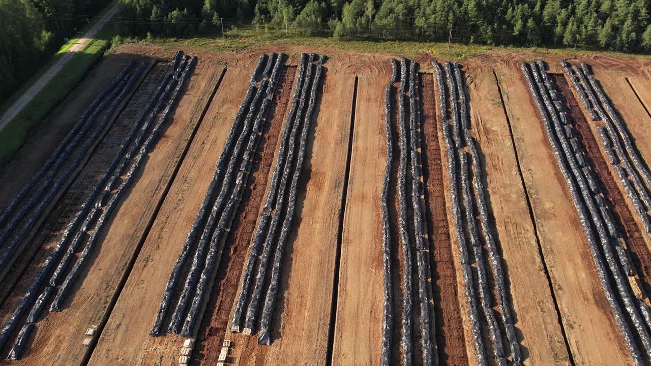 Aerial view of a large peat bog harvesting site with long parallel rows of extracted peat, wooden pallets, and covered stacks stretching across the landscape