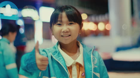 portrait of young little asiatic girl smiling in front of the camera showing the thumb up , blurred bokeh background