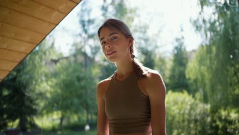 A-blonde-girl-in-a-light-brown-T-shirt-sits-against-the-backdrop-of-nature-in-the-gazebo,-looks-at-the-camera-and-smiles