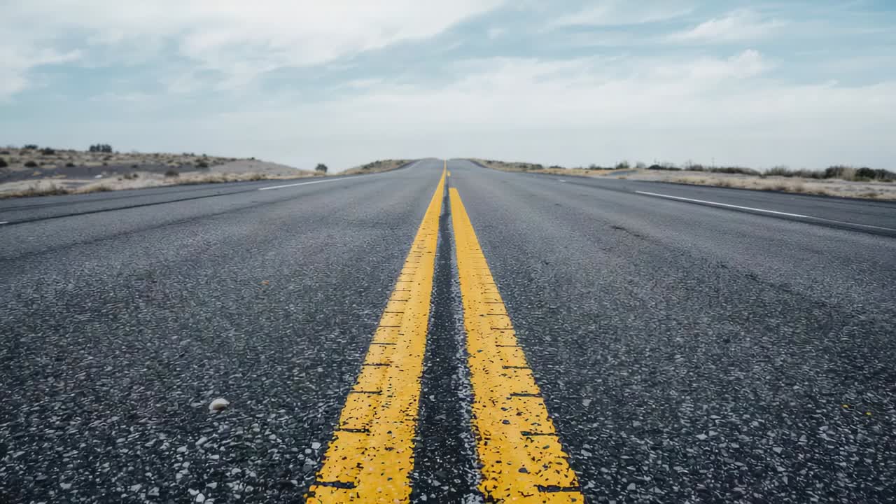 Panning low-angle camera advancing along desert road to reveal double yellow line and paint chips