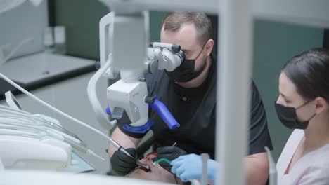 dentista masculino que trabaja con microscopio dental en la clínica moderna de estomatología. médico que utiliza el microscopio para el tratamiento del canal de la raíz. estomatólogo realiza una operación quirúrgica. odontología cosmética y cirugía.
