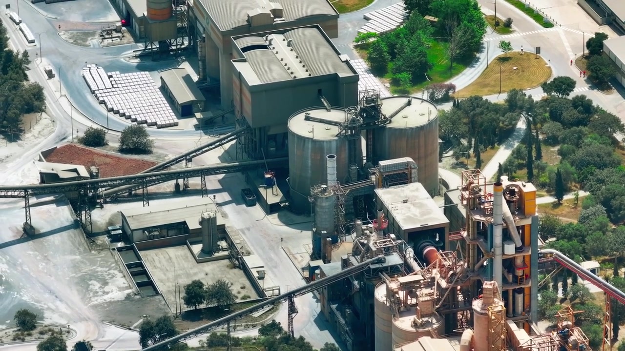 An aerial view of a cement production facility shows limestone quarry activities, aggregate processing, and heavy machinery in operation. Conveyor systems assist in material transport.