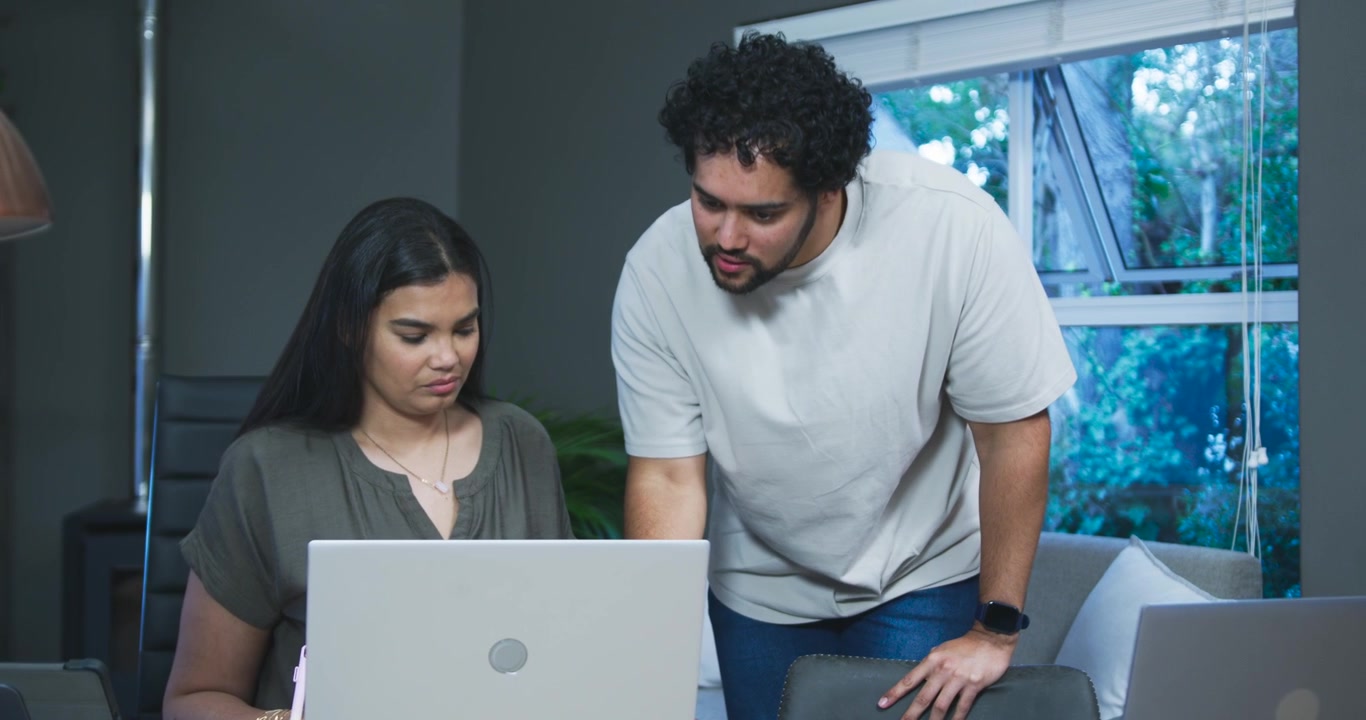 Equipo afroamericano en un escritorio, hombre llegando con un teléfono apuntando a una laptop y ayudando a una mujer que usa una tablet