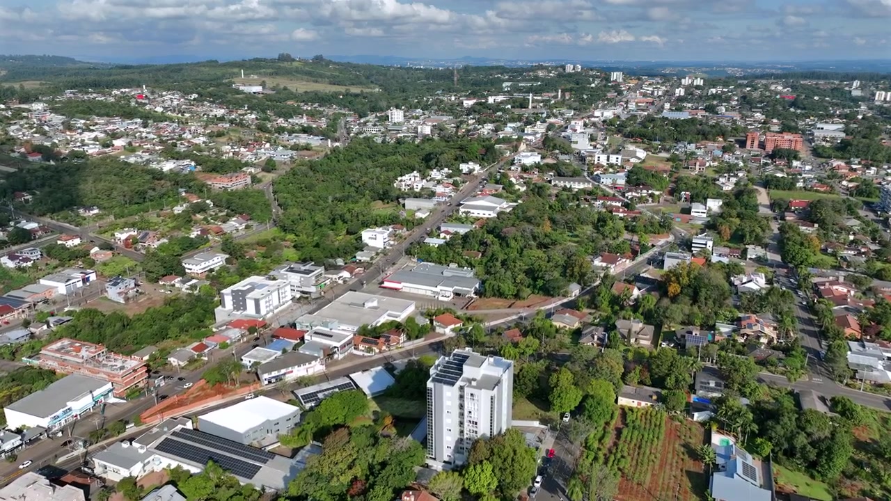 Ripresa aerea in avanti di un drone che rivela il viale principale di Ivoti, circondato da aree commerciali e residenziali con colline verdi in lontananza.