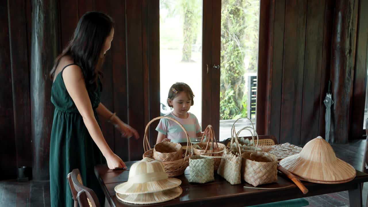 A loving Korean mother and her cute mixed daughter spend quality time together, exploring handmade woven baskets and hats during a cultural craft workshop at the JW Marriott Khao Lak resort