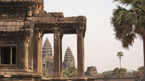 Weite-Zeitrafferaufnahme-Des-Windes-In-Den-Bäumen,-Der-Durch-Die-Säulen-Eines-Antiken-Denkmals-Auf-Zwei-Von-Drei-Türmen-Des-Tempels-Angkor-Wat-Blickt