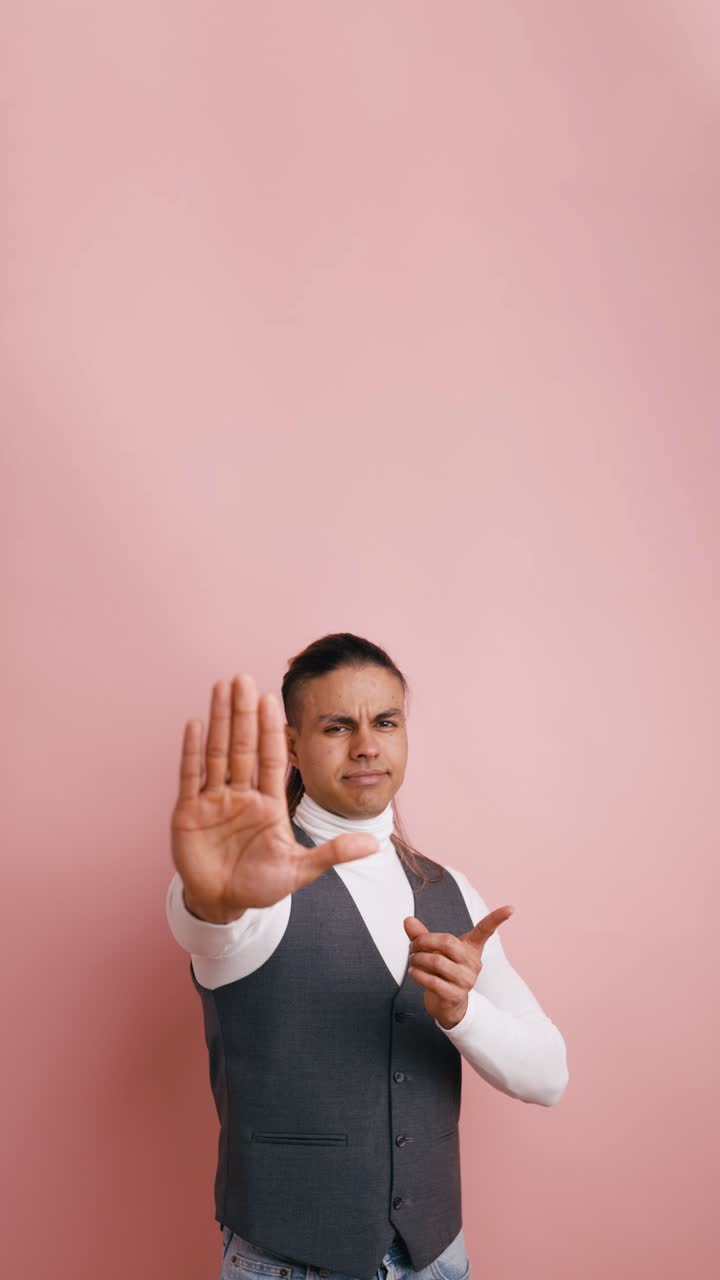 Uomo che fa un gesto di stop e avverte con il dito su sfondo rosa.