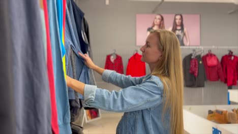 young caucasian woman looking at clothing, hanging on hangers. shopping in women’s clothing store. hd video