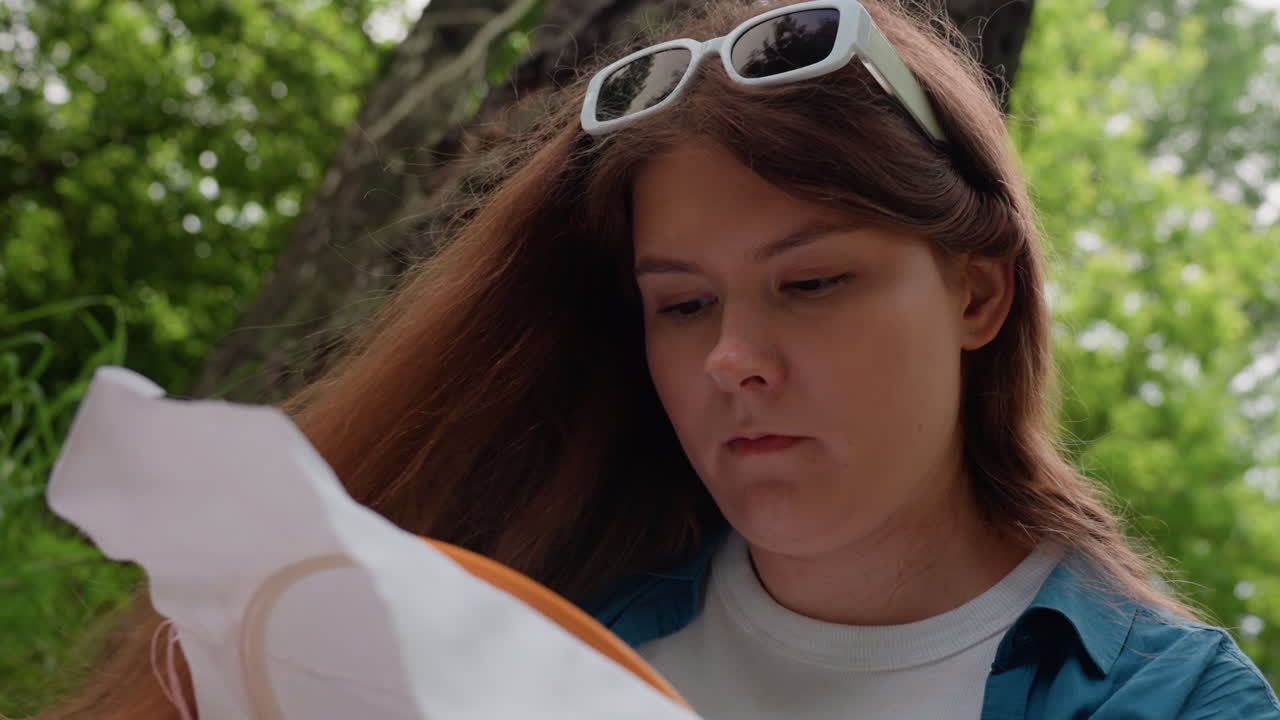 Close up of lady embroidering fabric outdoors with head slightly slanted, focused on precise handwork under natural light, showing calm concentration, delicate movement