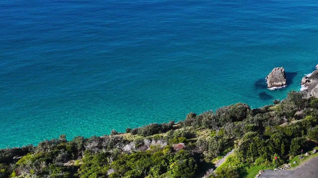 Des images de drone balayent des falaises verdoyantes et luxuriantes surplombant une eau bleue claire en Australie