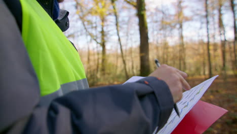 closeup shot of the worker while taking notes on his document at the clipboard in the middle of the forest, handheld