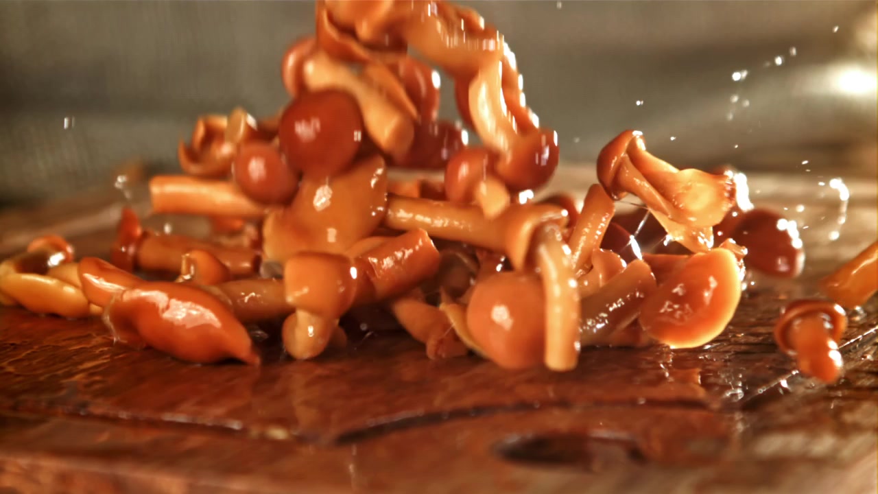 Funghi sott'aceto che cadono al rallentatore su un tagliere di legno bagnato