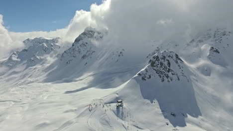 Aerial---Sky-high-view-of-skiers-on-mountain-with-cloud-covered-peak